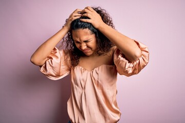 Naklejka premium Young beautiful woman with curly hair wearing casual t-shirt standing over pink background suffering from headache desperate and stressed because pain and migraine. Hands on head.