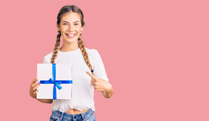 Beautiful caucasian woman with blonde hair holding gift smiling happy pointing with hand and finger