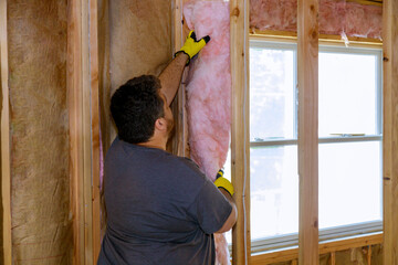 Construction worker thermally insulating layer under house with glass wool
