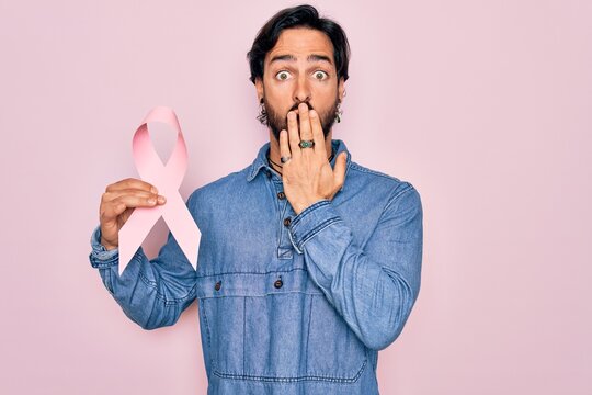 Young handsome hispanic man holding breast cancer awareness pink ribbon cover mouth with hand shocked with shame for mistake, expression of fear, scared in silence, secret concept