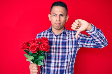 Young handsome latin man holding flowers with angry face, negative sign showing dislike with thumbs...