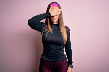 Young blonde fitness woman wearing sport workout clothes over isolated background covering eyes with hand, looking serious and sad. Sightless, hiding and rejection concept