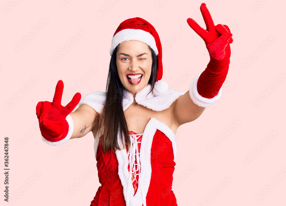 Poster young beautiful caucasian woman wearing santa claus costume smiling with tongue out showing fingers 