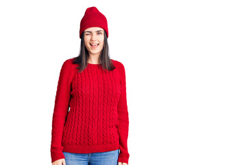 Young beautiful girl wearing sweater and wool cap winking looking at the camera with sexy expression, cheerful and happy face.