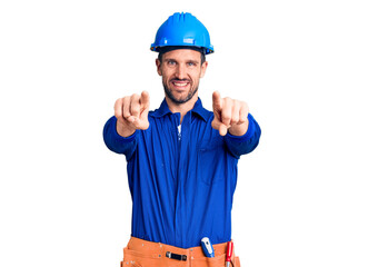 Young handsome man wearing worker uniform and hardhat pointing to you and the camera with fingers, smiling positive and cheerful