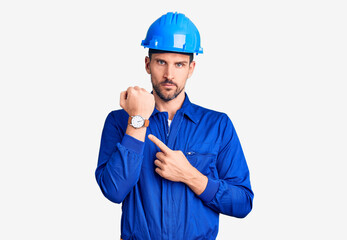Young handsome man wearing worker uniform and hardhat checking the time on wrist watch, relaxed and confident