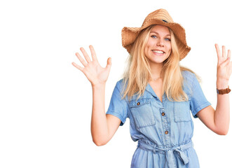 Young beautiful blonde woman wearing summer hat and dress showing and pointing up with fingers...