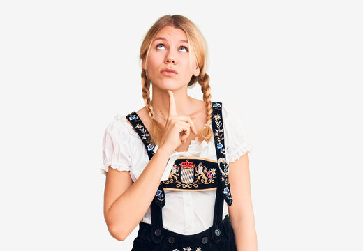 Young beautiful blonde woman wearing oktoberfest dress thinking concentrated about doubt with finger on chin and looking up wondering