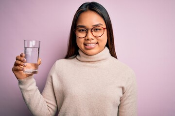 Young asian girl drinking glass of water to refreshment over isolated pink background with a happy face standing and smiling with a confident smile showing teeth