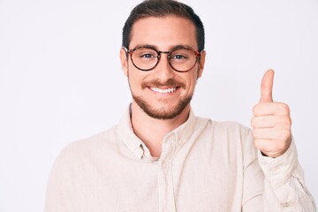Fototapeta premium Young handsome man wearing casual clothes and glasses smiling happy and positive, thumb up doing excellent and approval sign