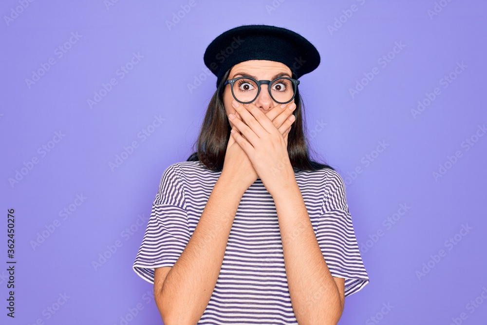 Sticker Young beautiful brunette woman wearing glasses and french beret over purple background shocked covering mouth with hands for mistake. Secret concept.