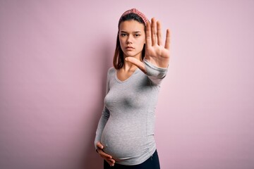 Young beautiful teenager girl pregnant expecting baby over isolated pink background doing stop sing with palm of the hand. Warning expression with negative and serious gesture on the face.