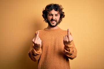 Naklejka premium Young handsome man with beard wearing casual sweater standing over yellow background Showing middle finger doing fuck you bad expression, provocation and rude attitude. Screaming excited