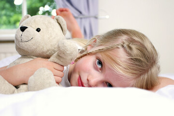 A girl lying down on the bed hugging a teddy bear