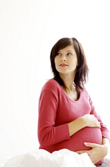 A pregnant lady sitting on the bed touching her stomach