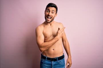 Young handsome strong man with beard shirtless standing over isolated pink background cheerful with a smile on face pointing with hand and finger up to the side with happy and natural expression