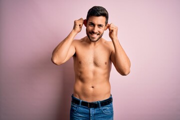 Fototapeta premium Young handsome strong man with beard shirtless standing over isolated pink background Smiling pulling ears with fingers, funny gesture. Audition problem