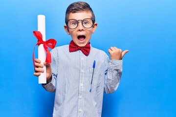 Cute blond kid wearing nerd bow tie and glasses holding diploma pointing thumb up to the side...