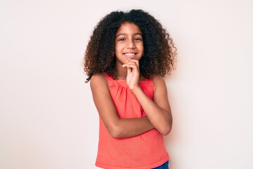 Fototapeta na wymiar African american child with curly hair wearing casual clothes smiling looking confident at the camera with crossed arms and hand on chin. thinking positive.