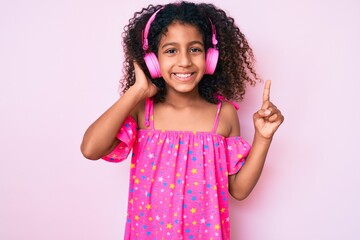 African american child with curly hair listening to music using headphones smiling with an idea or question pointing finger with happy face, number one