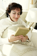 A lady sitting on the bed reading a book