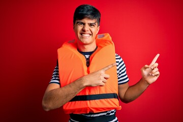 Young handsome man wearing orange safety life jacket over isolated red background smiling and...