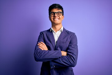 Young handsome business man wearing jacket and glasses over isolated purple background happy face smiling with crossed arms looking at the camera. Positive person.