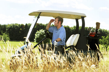 A guy sitting in a golf cart looking for his golf ball