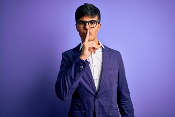 Obraz premium Young handsome business man wearing jacket and glasses over isolated purple background asking to be quiet with finger on lips. Silence and secret concept.