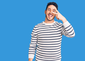 Young hispanic man wearing casual clothes doing peace symbol with fingers over face, smiling cheerful showing victory