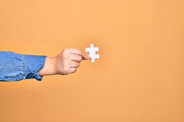 Fototapeta na wymiar Hand of caucasian young woman holding piece of puzzle over isolated yellow background