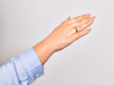Hand of caucasian young woman holding golden marriage ring over isolated white background