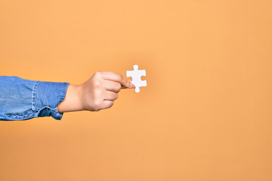 Hand of caucasian young woman holding piece of puzzle over isolated yellow background