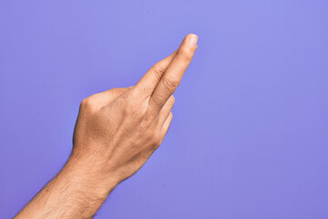 Hand of caucasian young man showing fingers over isolated purple background gesturing fingers crossed, superstition and lucky gesture, lucky and hope expression