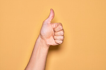 Hand of caucasian young man showing fingers over isolated yellow background doing successful approval gesture with thumbs up, validation and positive symbol
