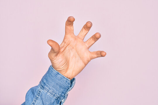 Hand of caucasian young man showing fingers over isolated pink background grasping aggressive and scary with fingers, violence and frustration