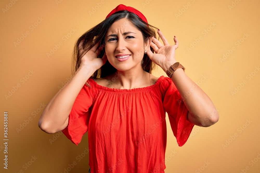 Wall mural Young beautiful woman colorful summer style over yellow isolated background Trying to hear both hands on ear gesture, curious for gossip. Hearing problem, deaf