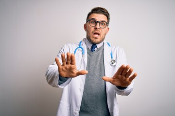 Young doctor man with blue eyes wearing medical coat and stethoscope over isolated background...