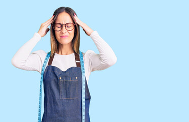 Beautiful brunette young woman dressmaker designer wearing atelier apron suffering from headache desperate and stressed because pain and migraine. hands on head.