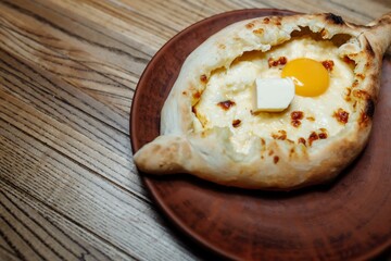 Top view on traditional Adjarian Khachapuri - open baked pie with melted salt cheese suluguni and egg yolk on wooden tray. Traditional georgian food