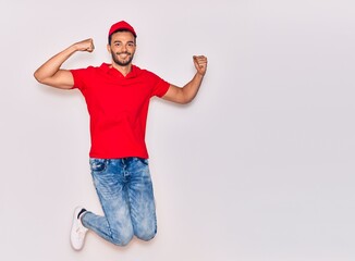 Young handsome hispanic deliveryman wearing uniform smiling happy. Jumping with smile on face celebrating with fists up over isolated white background.