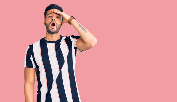 Young handsome hispanic man wearing striped tshirt surprised with hand on head for mistake, remember error. forgot, bad memory concept.