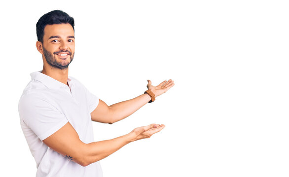 Young handsome hispanic man wearing casual clothes inviting to enter smiling natural with open hand