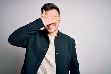 Young handsome business mas wearing elegant winter coat standing over isolated background smiling and laughing with hand on face covering eyes for surprise. Blind concept.