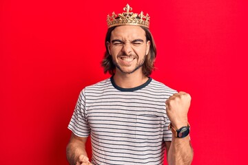 Young handsome man wearing prince crown celebrating surprised and amazed for success with arms...