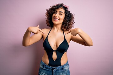 Young beautiful arab woman on vacation wearing swimsuit and sunglasses over pink background looking...