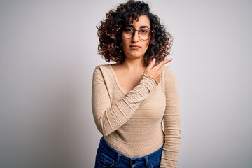 Young beautiful curly arab woman wearing casual t-shirt and glasses over white background Pointing with hand finger to the side showing advertisement, serious and calm face