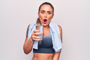 Beautiful blonde sporty woman using towel drinking bottle of water over white background scared and...