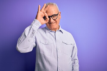Middle age handsome hoary man wearing striped shirt and glasses over purple background doing ok gesture with hand smiling, eye looking through fingers with happy face.