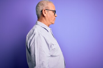 Middle age handsome hoary man wearing striped shirt and glasses over purple background looking to side, relax profile pose with natural face with confident smile.